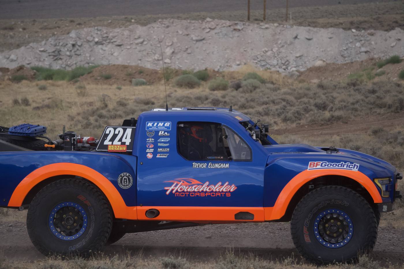 A blue and orange race truck against desert scrub