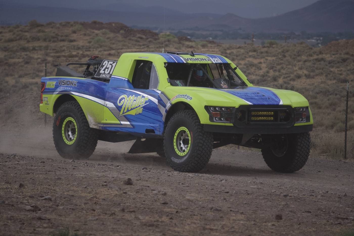 A lime green and blue race truck kicking up dust