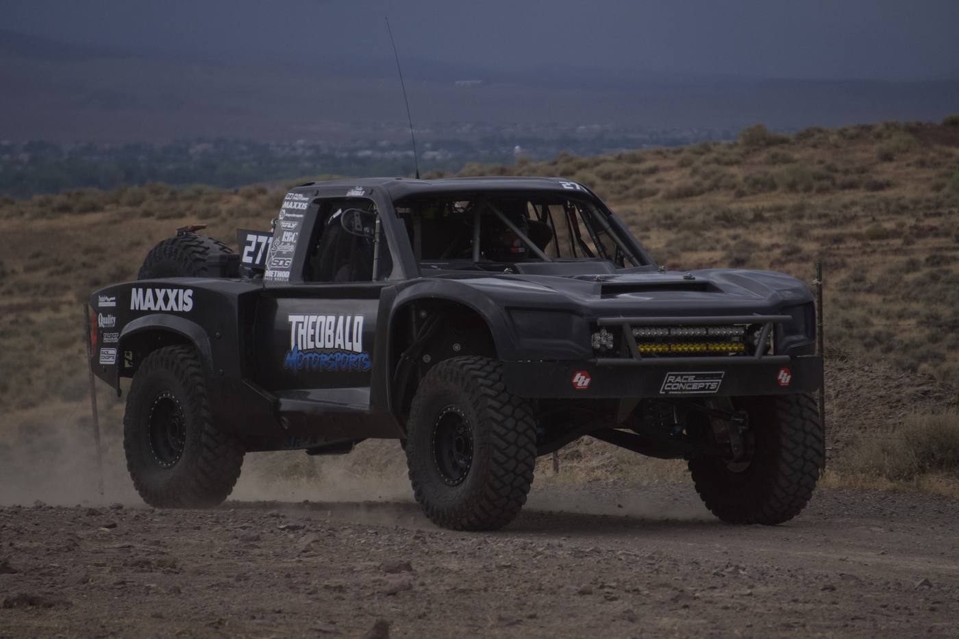 A black race truck coming head-on out of its own dust