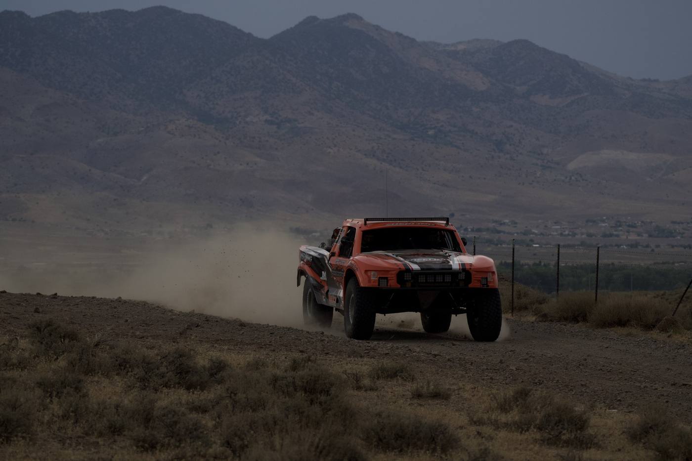 A small orange truck dwarfed by the Nevada mountains