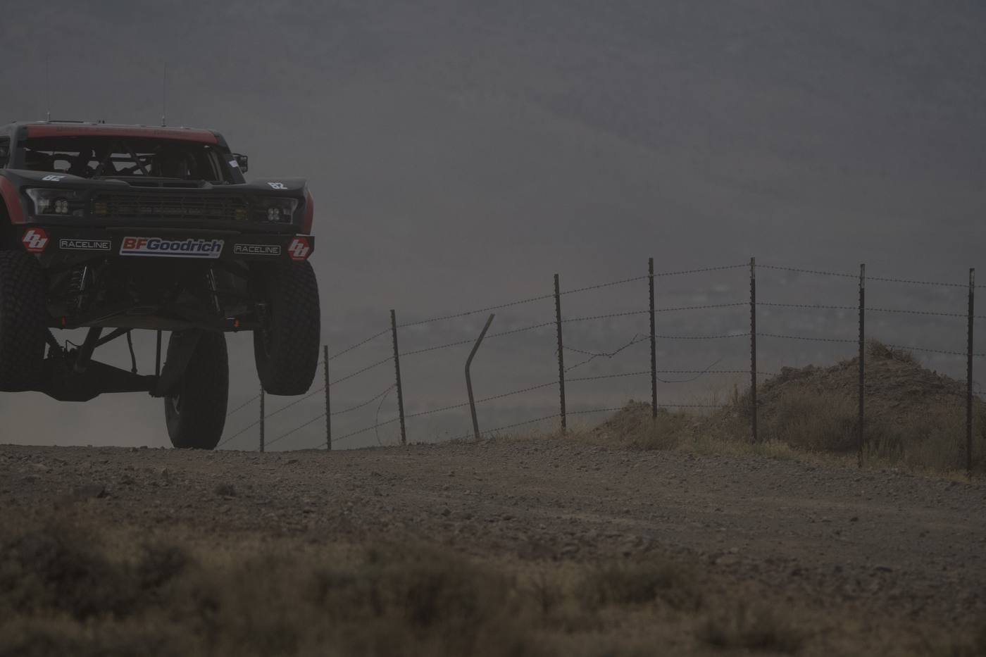 A race truck silhouetted mid-air in thick dust haze